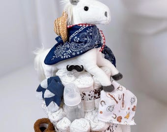 May include: A white plush horse wearing a blue bandana and a straw hat sits atop a diaper cake decorated with cowboy-themed fabric and a bottle. The cake is surrounded by brown plush horse booties.