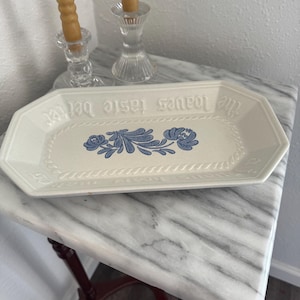 May include: A white ceramic mug with a black handle and the text "But First, Coffee" in a bold, black font. The mug is set against a blurred background, suggesting a cozy setting.