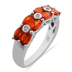 May include: A silver band ring with five oval-shaped orange gemstones and small clear gemstones set in the band.