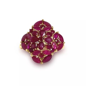 May include: A gold ring featuring a cluster of oval-cut rubies. The rubies are a deep red-pink hue and are set closely together, creating a textured, floral-like design. The ring's band is a polished gold.