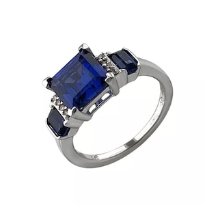 May include: A silver ring with a large, square, blue gemstone surrounded by smaller, clear gemstones. The ring has a simple band.
