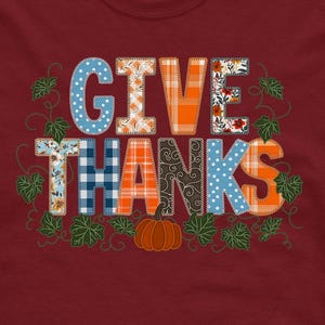 Könnte beinhalten: Ein weinrotes T-Shirt mit dem Schriftzug "GIVE THANKS" in einem Patchwork-Design, einem Kürbis und Blättern. Der Text "MOCKUP ONLY" ist unten in Weiß aufgedruckt. Das Design enthält orange, blaue und florale Muster.