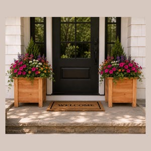 May include: Two square wooden planters with four legs each, filled with vibrant pink, purple, and orange flowers and green foliage. A rectangular brown coir doormat with a black border and the word WELCOME printed in black sits between them.