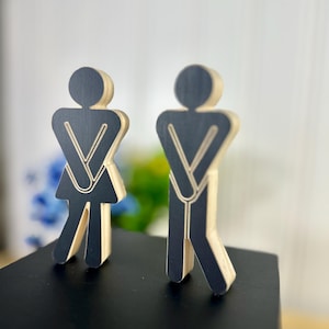 May include: Two wooden figures, one with arms crossed and the other with hands on hips, are standing on a black surface. The figures are black with a wood grain texture.