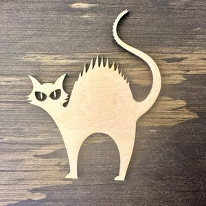 May include: A wooden cutout of a cat with an arched back, spiky fur, and a curved tail. The cat has pointed ears and angry eyes. The cat is light brown and sits on a dark brown wooden surface. A Halloween decoration.