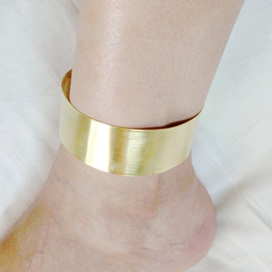 May include: A gold-toned ankle bracelet with a wide, flat band.