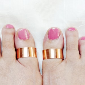 May include: Two copper toe rings on a pair of feet with pink nail polish.