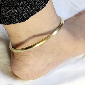 May include: A simple gold ankle bracelet made of a single, thick band of metal.