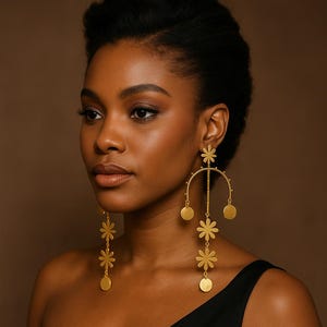 May include: Gold-colored statement earrings featuring a floral and circular design. The earrings have a long, dangling style with multiple flower and disc-shaped elements. The earrings are worn by a person wearing a black top.