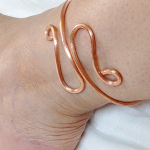 May include: A copper ankle bracelet with a simple, elegant design. The bracelet is made of a single piece of wire that is twisted and shaped into a delicate pattern.