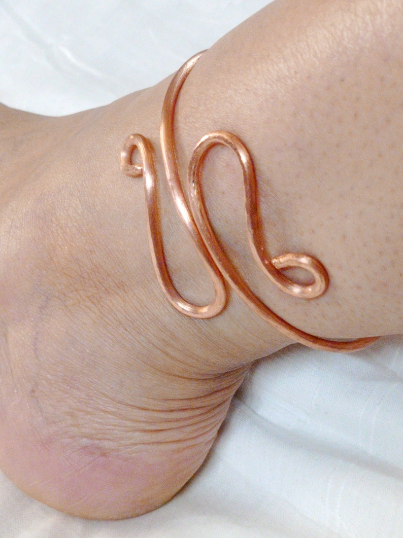May include: A copper ankle bracelet with a simple, elegant design. The bracelet is made of a single piece of wire that is twisted and shaped into a delicate pattern.