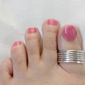 Può includere: Primo piano di un piede con smalto rosa sulle dita. L'alluce ha un anello per dita dei piedi in argento con più bande.