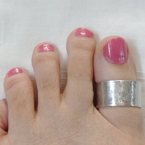 May include: A silver toe ring with a hammered finish. The ring is worn on the big toe of a foot with pink nail polish.