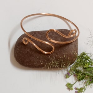 May include: A copper wire bracelet with a simple, wavy design. The bracelet is resting on a brown rock.