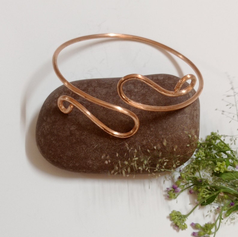 May include: A copper wire bracelet with a simple, wavy design. The bracelet is resting on a brown rock.