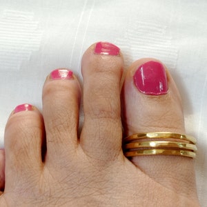Puede incluir: Primer plano de un pie con un anillo de dedo del pie de oro. El dedo del pie está pintado con esmalte de uñas rosa.
