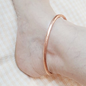 Könnte beinhalten: Ein schlichtes, gehämmertes Fußkettchen aus Kupfer. Das Armband besteht aus einem einzigen, dünnen Kupferband.