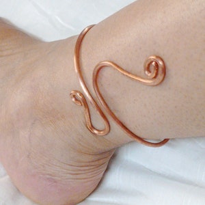 Pode incluir: Um bracelete de tornozelo de cobre com um design em espiral. O bracelete é feito de uma única peça de fio que é dobrada em uma forma única.