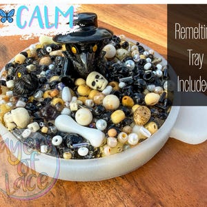 May include: A round, white tray filled with various beads, skulls, and a black plague doctor figurine. The tray has the word "CALM" in light blue and the text "Remelting Tray Included!"
