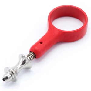 May include: A red wine bottle opener with a circular handle and a metal corkscrew. The opener has a spring mechanism and a decorative silver-colored metal design. The tool is designed for easy cork removal.
