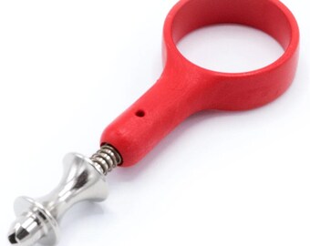 May include: A red wine bottle opener with a circular handle and a metal corkscrew. The opener has a spring mechanism and a decorative silver-colored metal design. The tool is designed for easy cork removal.