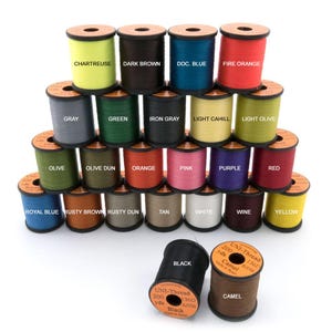 May include: A collection of colorful spools of thread in various shades, including chartreuse, dark brown, and fire orange. Each spool is labeled with its color name. The thread is used for crafts and sewing.