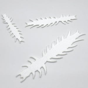 May include: Three white, spiky, feather-shaped craft foam cutouts. The cutouts vary in size and are arranged on a white background. The shapes have a textured, glittery appearance, suggesting they might be used for decorative purposes or craft projects.