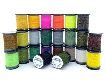 May include: A collection of spools of Semperfli fly tying thread in various colors, including gold, yellow, pink, orange, green, and brown. The spools are arranged in rows, with two spools in the foreground displaying product information.
