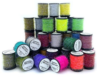 May include: A collection of colorful spools of Semperfli Straggle String, in shades of green, yellow, pink, purple, and silver. The spools are cylindrical and stacked, with labels visible on some. Ideal for crafting and fly tying.