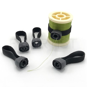 May include: A spool of green thread with a black band and several black elastic thread keepers. The thread keepers have a loop and a gray plastic piece. A strand of green thread extends from the spool.