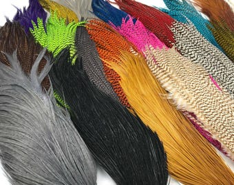 May include: A collection of colorful feathers in various shades, including gray, black, green, orange, pink, and brown. The feathers are arranged in a fan-like pattern, showcasing their diverse textures and hues. Ideal for crafting or decorative purposes.