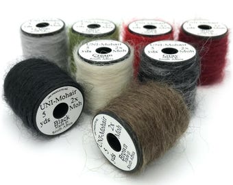 May include: A collection of mohair yarn spools in various colors, including black, brown, gray, red, and cream. Each spool has a label with the brand name, yardage, and fiber type. The yarn is made in South Africa.