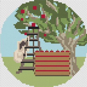 May include: A brown wooden ladder with a white bag hanging on the side, leaning against a green tree with red apples. A brown wooden crate with red apples sits in front of the ladder.