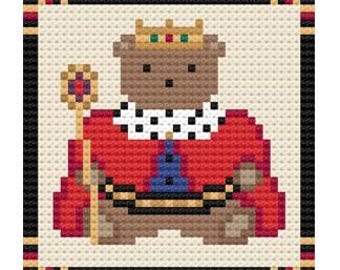May include: Cross-stitch pattern of a teddy bear king wearing a gold crown with red, green, and black accents. The bear is dressed in a red robe with a black and white collar, holding a gold scepter. The design is framed with a black border.