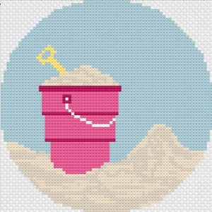 May include: A pink plastic bucket filled with sand and a yellow plastic shovel. The bucket is sitting on a sandy beach.