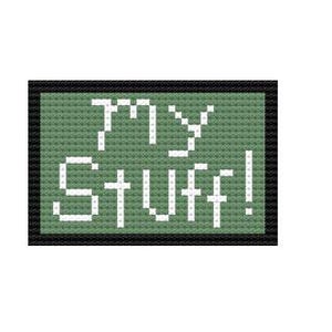 Op de afbeelding: Een kruissteekontwerp op een groene achtergrond met de woorden "MY STUFF!" in het wit. De tekst is in een pixelachtige lettertype en het ontwerp is omlijst door een zwarte rand. De algehele esthetiek doet denken aan retro videogames.
