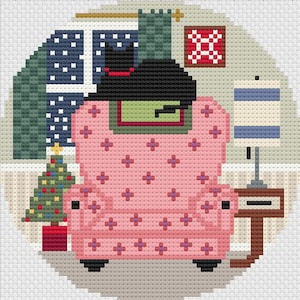 May include: A black cat sits in a pink armchair with a green and red patterned throw. A small Christmas tree with colorful ornaments is in the corner. The room has a blue and white window with snowflakes, a green curtain, and a red and white quilt hanging on the wall.