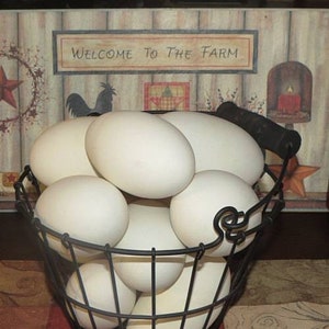 May include: A wire basket filled with large, white eggs. The basket has a black handle and is set against a rustic wooden background with the text "WELCOME TO THE FARM". A decorative star and rooster silhouette are also visible.
