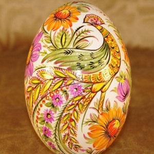 May include: A hand-painted decorative egg featuring a peacock design. The egg is adorned with vibrant floral patterns in shades of orange, pink, yellow, and green against a white background. The peacock is depicted with intricate details, adding to the egg's artistic appeal.