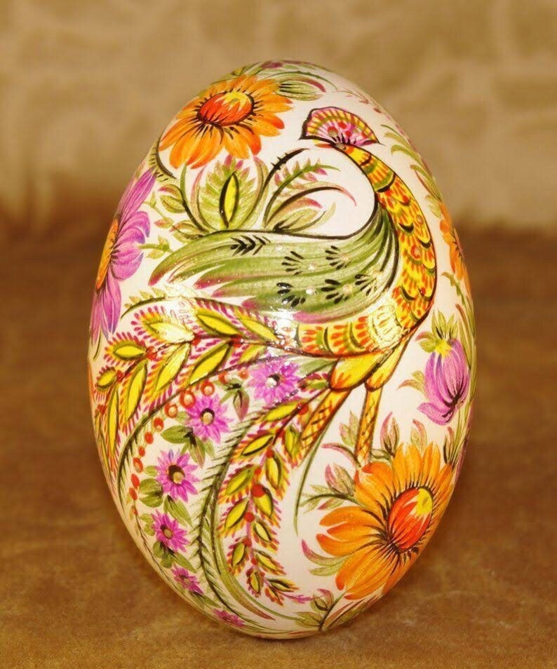 May include: A hand-painted decorative egg featuring a peacock design. The egg is adorned with vibrant floral patterns in shades of orange, pink, yellow, and green against a white background. The peacock is depicted with intricate details, adding to the egg's artistic appeal.