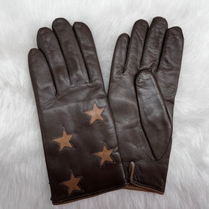 Könnte beinhalten: Ein Paar braune Lederhandschuhe mit beigefarbenen Stern-Applikationen.