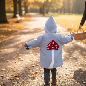 May include: A light blue hooded coat featuring a large red and white mushroom appliqué on the back. The coat has long sleeves with patterned cuffs, and it is worn over dark gray pants and brown boots, creating a functional outer garment.