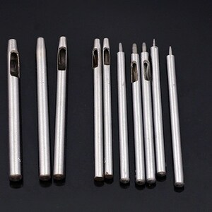 May include: A set of 12 silver metal leather hole punches of varying sizes. The punches are arranged in a row on a black surface.