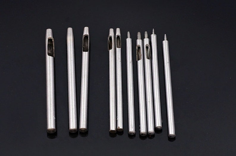 May include: A set of 12 silver metal leather hole punches of varying sizes. The punches are arranged in a row on a black surface.