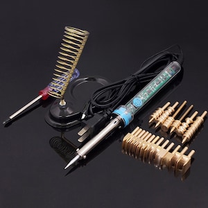 Könnte beinhalten: Ein Lötkolben-Set mit einem blau-schwarzen Lötkolben, einem schwarzen Ständer mit einer Spiralfeder und einem Satz von 12 goldfarbenen Metallspitzen.