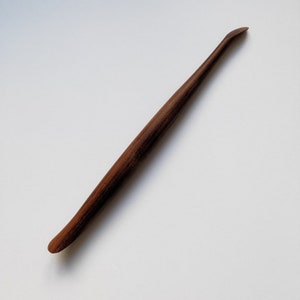 May include: A wooden tool with a curved handle and a pointed tip. The tool is brown and has a natural wood finish.