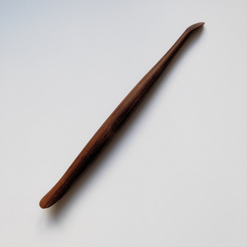 May include: A wooden tool with a curved handle and a pointed tip. The tool is brown and has a natural wood finish.