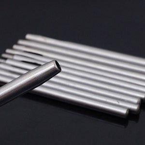 May include: A set of ten silver metal leather hole punches. The punches are arranged in a stack, with the largest punch at the top and the smallest punch at the bottom. The punches are used to create holes in leather for sewing or other purposes.