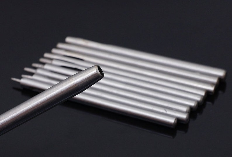 May include: A set of ten silver metal leather hole punches. The punches are arranged in a stack, with the largest punch at the top and the smallest punch at the bottom. The punches are used to create holes in leather for sewing or other purposes.