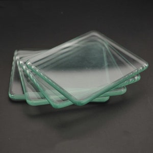 May include: Four clear glass squares stacked on top of each other. The glass has a slightly green tint and polished edges.